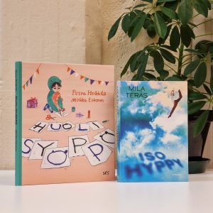 Huolisyöppö-kirja ja Iso hyppy -kirja vierekkäin pystyssä pöydällä.