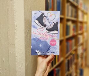 Sulamispiste kirja kädessä kirjahyllyn edessä.