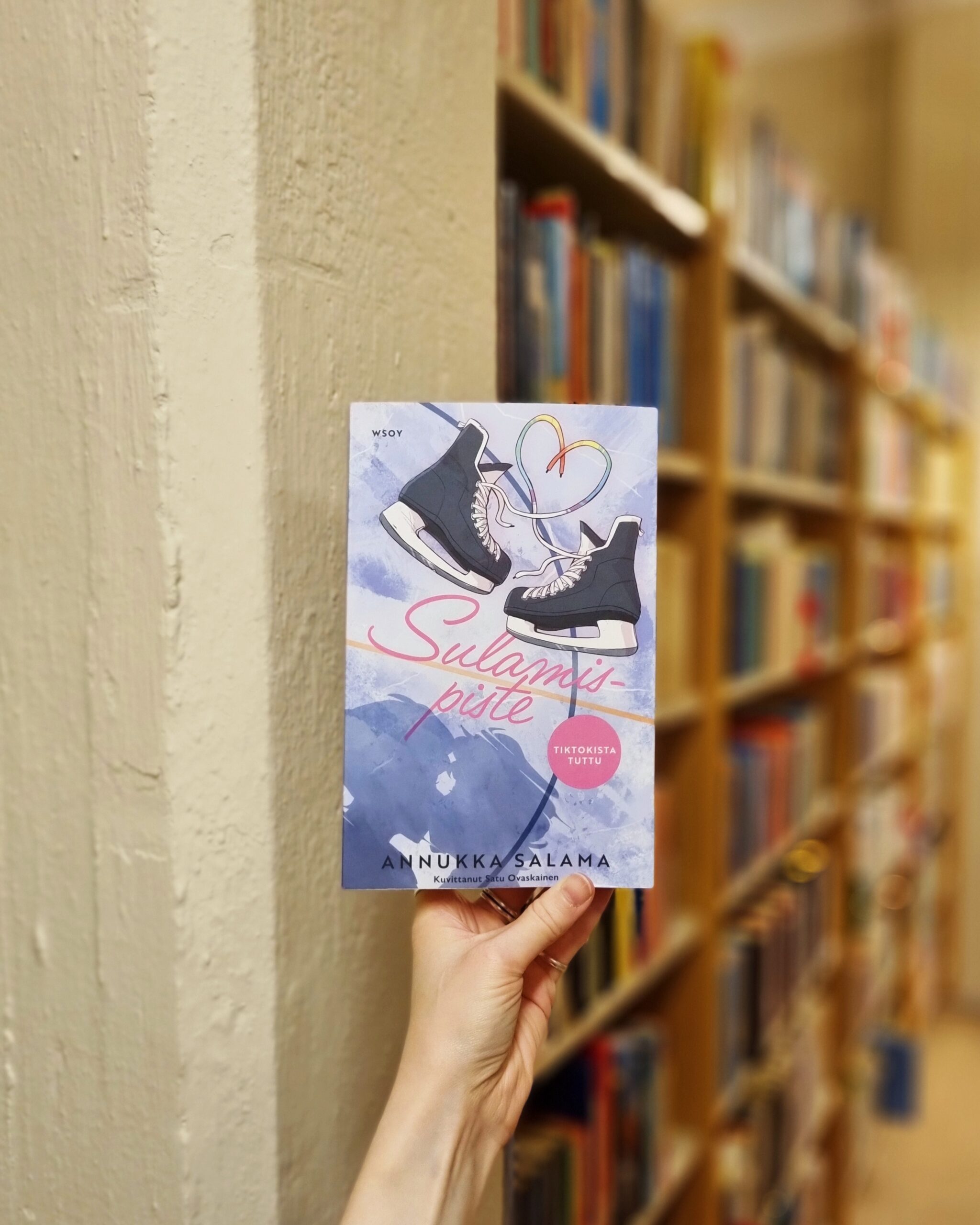 Sulamispiste kirja kädessä kirjahyllyn edessä.
