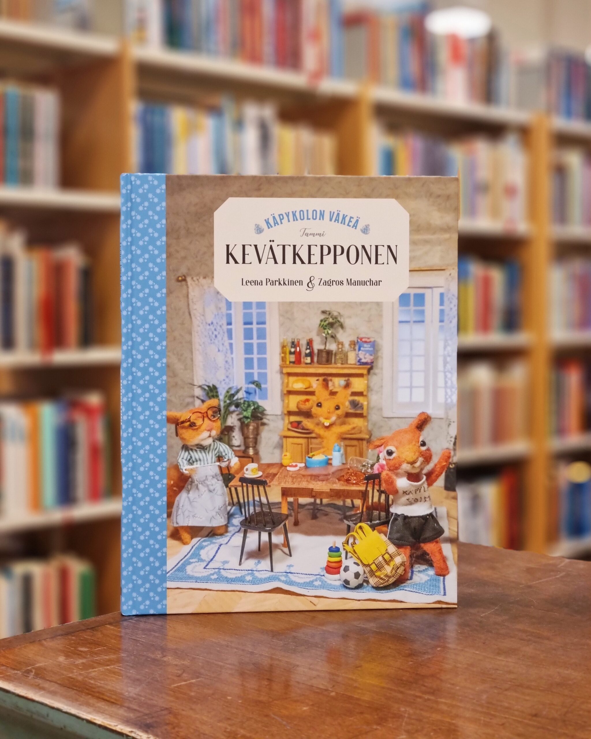 Kuvassa Kevätkepponen kirja, taustalla kirjahyllyjä.