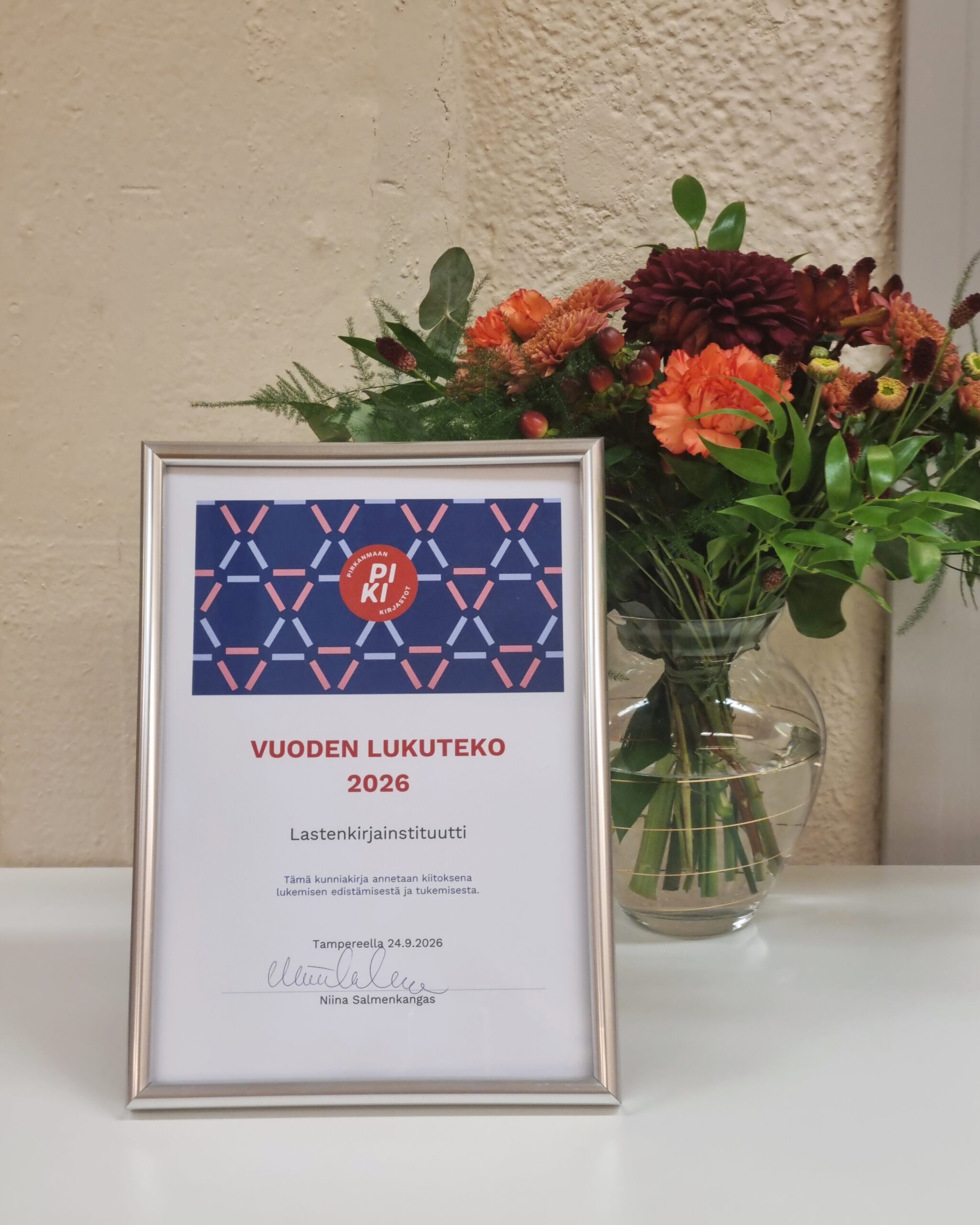 Vuoden lukuteko -kunniakirja ja kukkakimppu maljakossa.